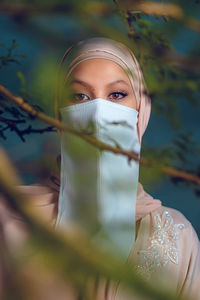 Portrait of veiled woman with white niqab and hijab standing behind the tree