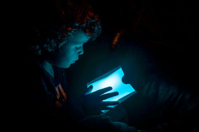 Close-up of boy holding illuminated light in darkroom