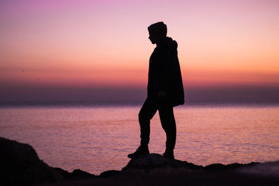 Silhouette man standing at beach against sky during sunset