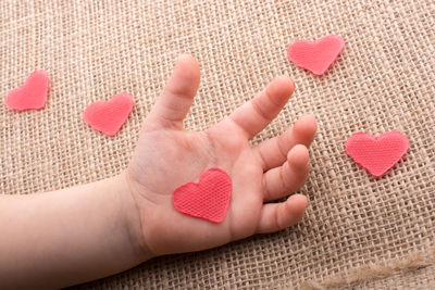 Cropped hand of child with red heart shape on table