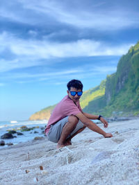 Full length of young man on sand at beach against sky