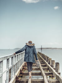 Rear view of man standing on pier over sea against sky
