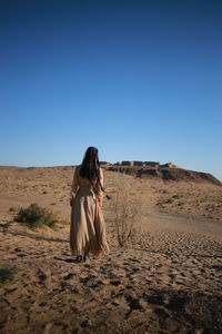 Woman standing on desert against clear sky