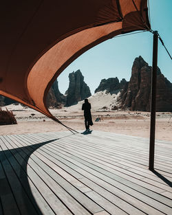 Rear view of teenage girl standing on desert against rock mountains