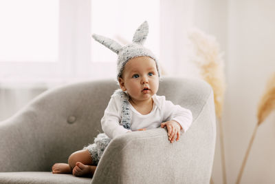 Cute baby wearing bunny cap looking away while sitting on sofa