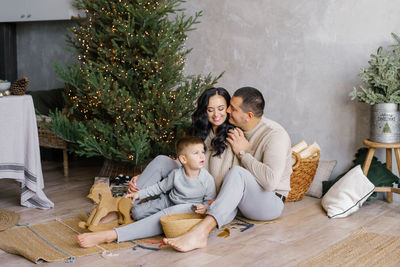 A stylish young beautiful family with a young son is playing on the floor near the christmas tree 