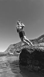 Young woman on rock by sea against clear sky