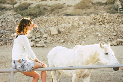 Woman sitting by pony on railing in ranch