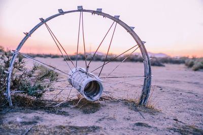 Abandoned wheel on sand against clear sky during sunset
