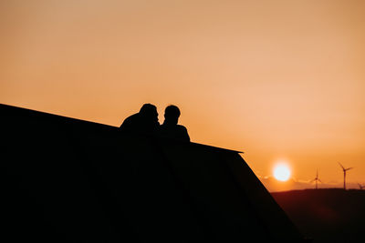 Silhouette people on roof against orange sky