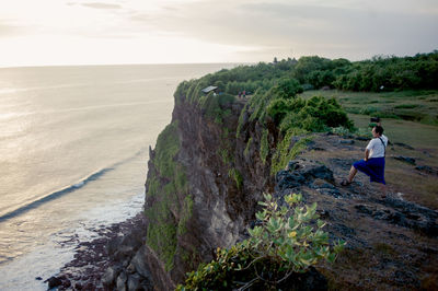 Mature man photographing sea while standing on mountain during sunset