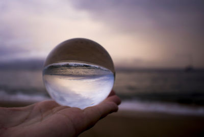 Close-up of hand holding crystal ball against sea