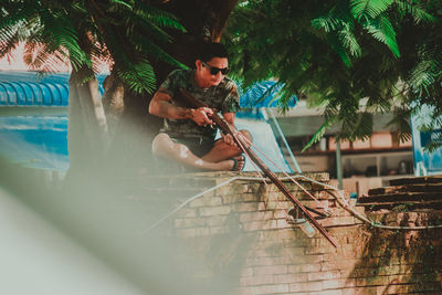 Man photographing with mobile phone by tree