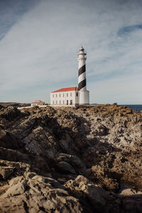 Lighthouse on cliff by sea against sky