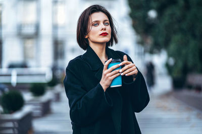 Young woman holding smart phone while standing on camera