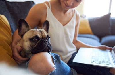 Smiling woman playing with dog while using laptop at home