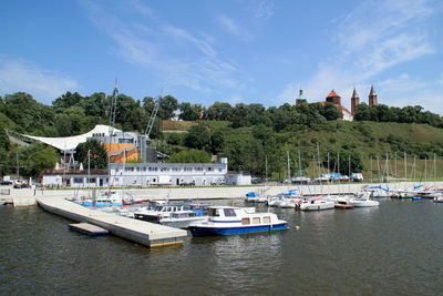 Sailboats moored on river by buildings against sky