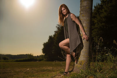 Full length portrait of young woman leaning against tree trunk
