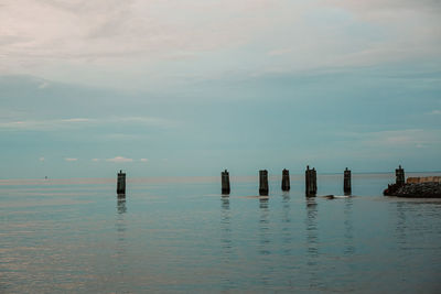 Wooden posts in sea against sky