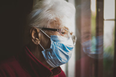 Close-up of senior woman wearing mask with reflection on window