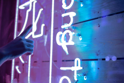 Cropped hand of person pointing at illuminated text on wall