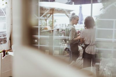 Rear view of businesswomen standing in restaurant seen through glass window