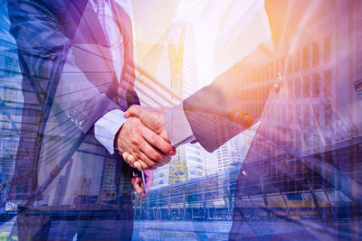 Digital composite image of businessmen shaking hands against buildings and footbridge in city