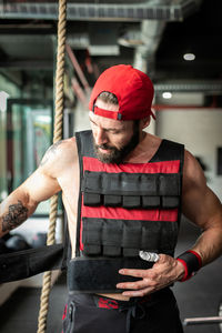 Focused male athlete putting on heavy weight vest for intense training in modern sports club