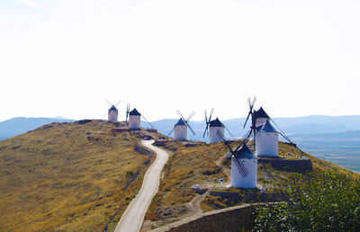 Road and traditional windmills on hill against clear sky during sunny day