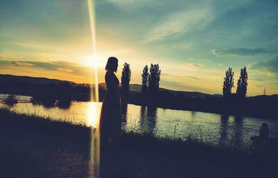 Silhouette people standing by lake against sky during sunset