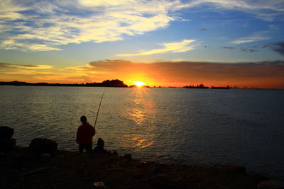 Silhouette men fishing in sea against sky during sunset