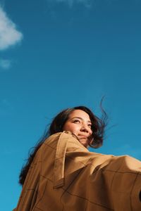 Low angle portrait of woman standing against blue sky