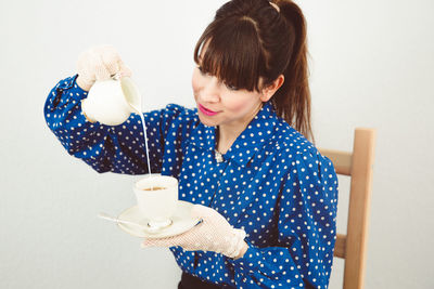 Mid adult woman pouring milk in coffee at home