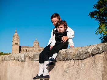 Portrait cute siblings sitting on wall against historic building