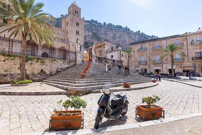 People walking around duomo di cefalù with rocca di cefalù in sicily on a sunny day - angled view.