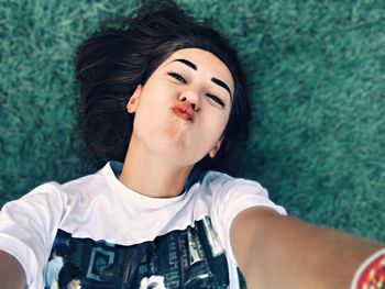 High angle view portrait of young woman taking selfie while lying on grass