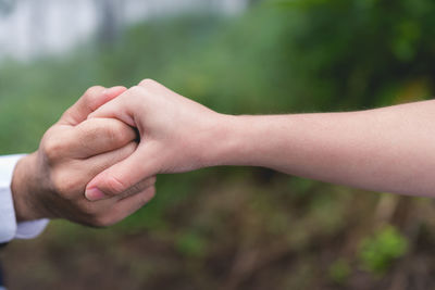Cropped image of couple holding hands at field