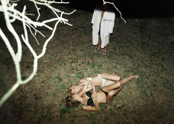 High angle view of lesbians romancing while man standing on field at night
