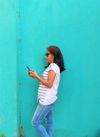 Woman using phone while standing against wall