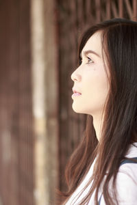 Side view of thoughtful young woman standing by closed gate