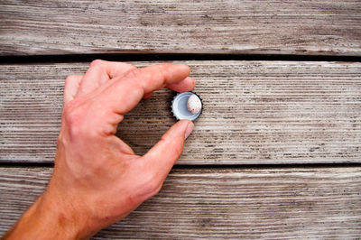 Cropped hand of man holding bottle cap on wooden table