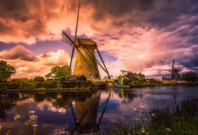 Traditional windmill by lake against cloudy sky