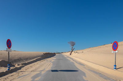 Road sign in desert against clear blue sky