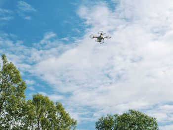 Low angle view of drone flying against cloudy sky