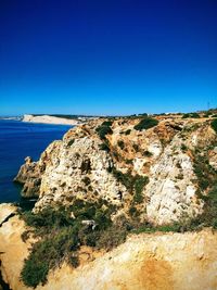 Scenic view of rocks in sea against clear blue sky