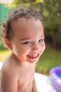 Happy kid playing in an inflatable pool in backyard. curly toddler smiling and playing with water