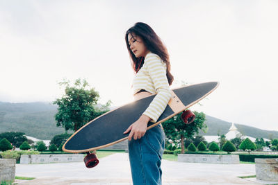 Young woman holding skateboard while standing on street