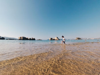 Boy wading in sea against clear sky