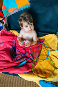 High angle view of boy holding shuttlecock while sitting in suitcase