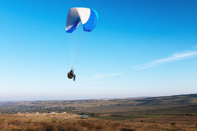 A paraglider takes off from a mountainside with a blue and white canopy and the sun behind. a